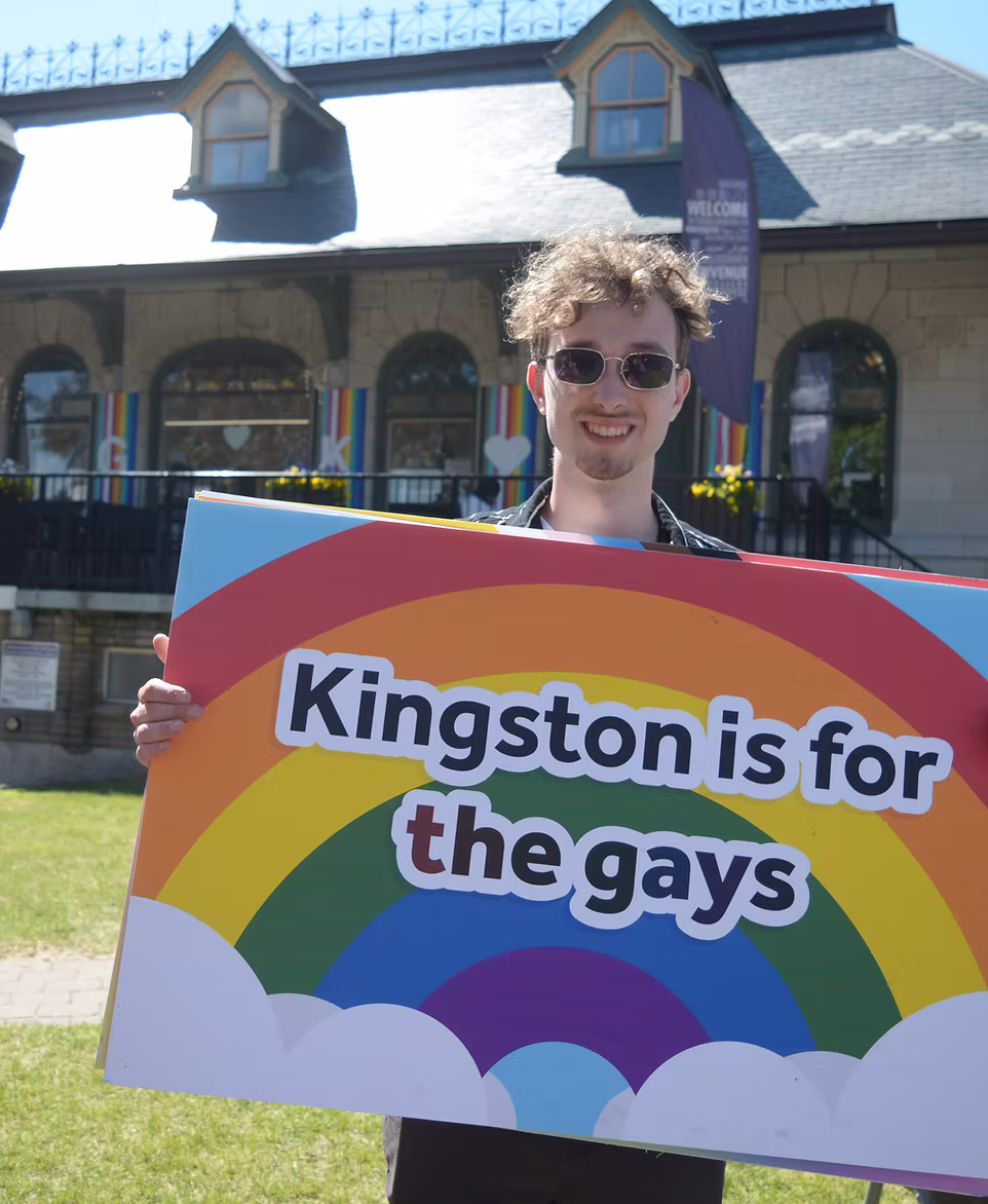 Person smiling holding sign with rainbow that says Kingston is for the gays